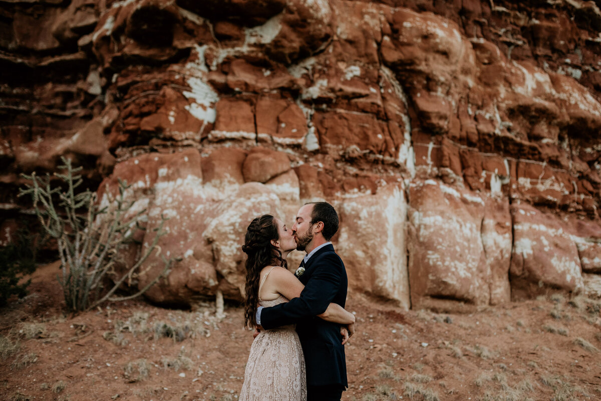 eloping couple kissing in front of red rocks