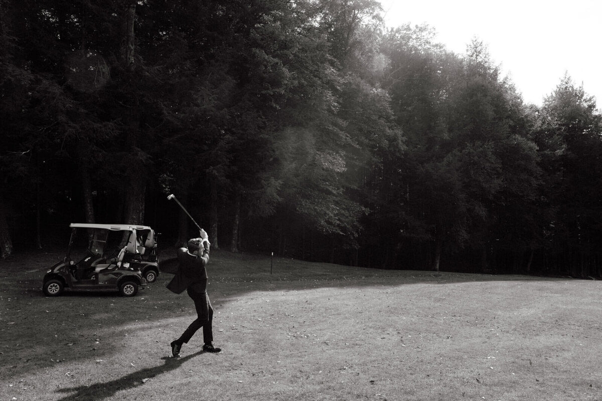 Black and white photo of the groom playing golf at The Ausable Club, NY. Image by Jenny Fu Studio.