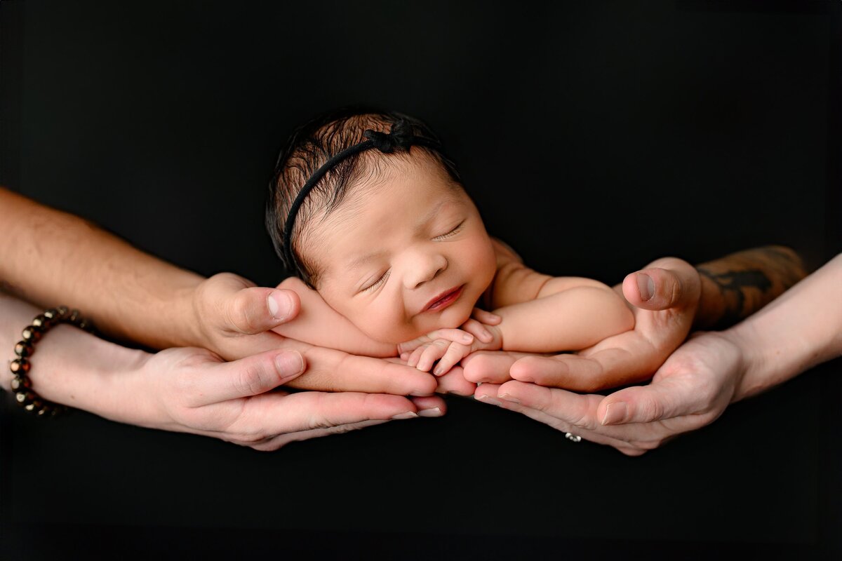 parent hands hoolding newborn baby girl wearing a black bow on black background