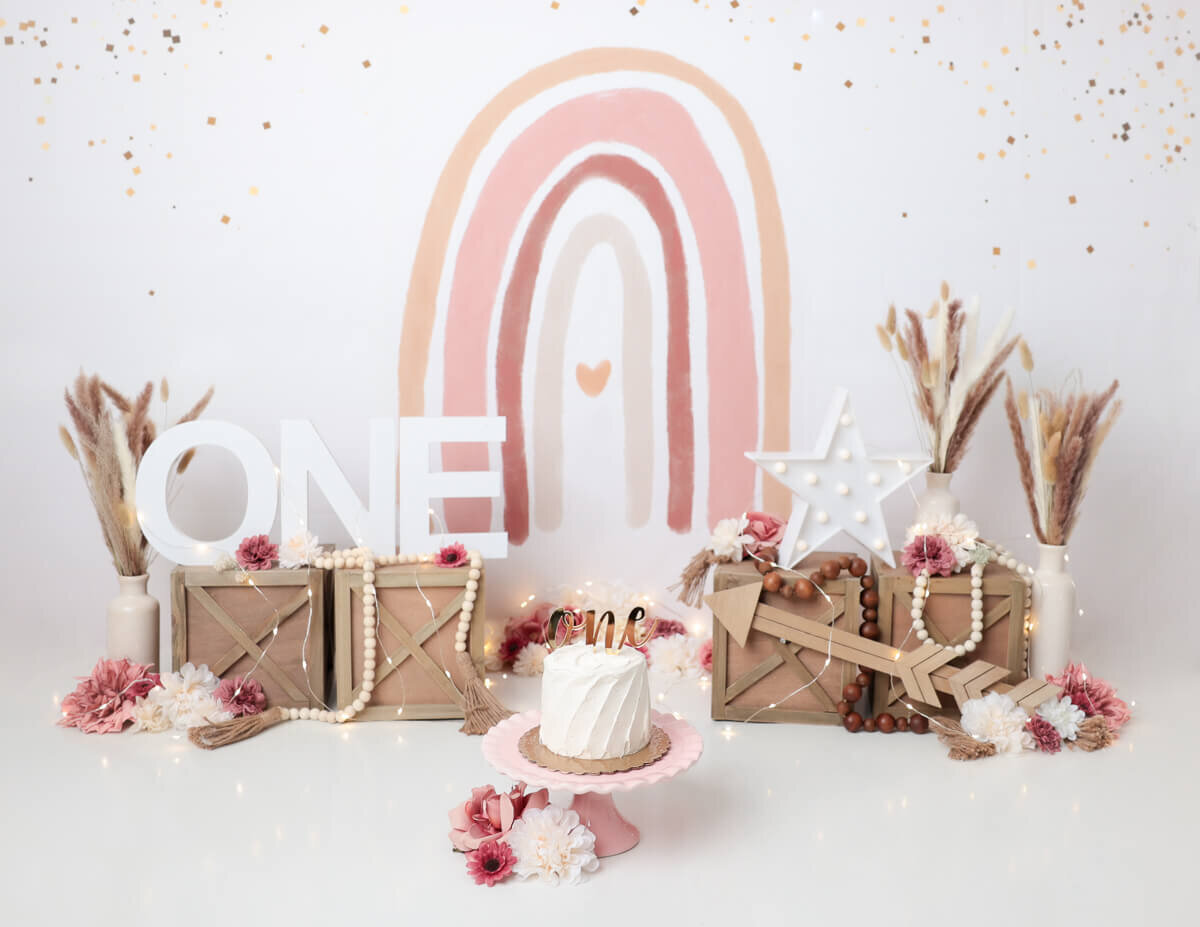 A boho-themed cake smash in Rochester, NY with a rainbow backdrop.