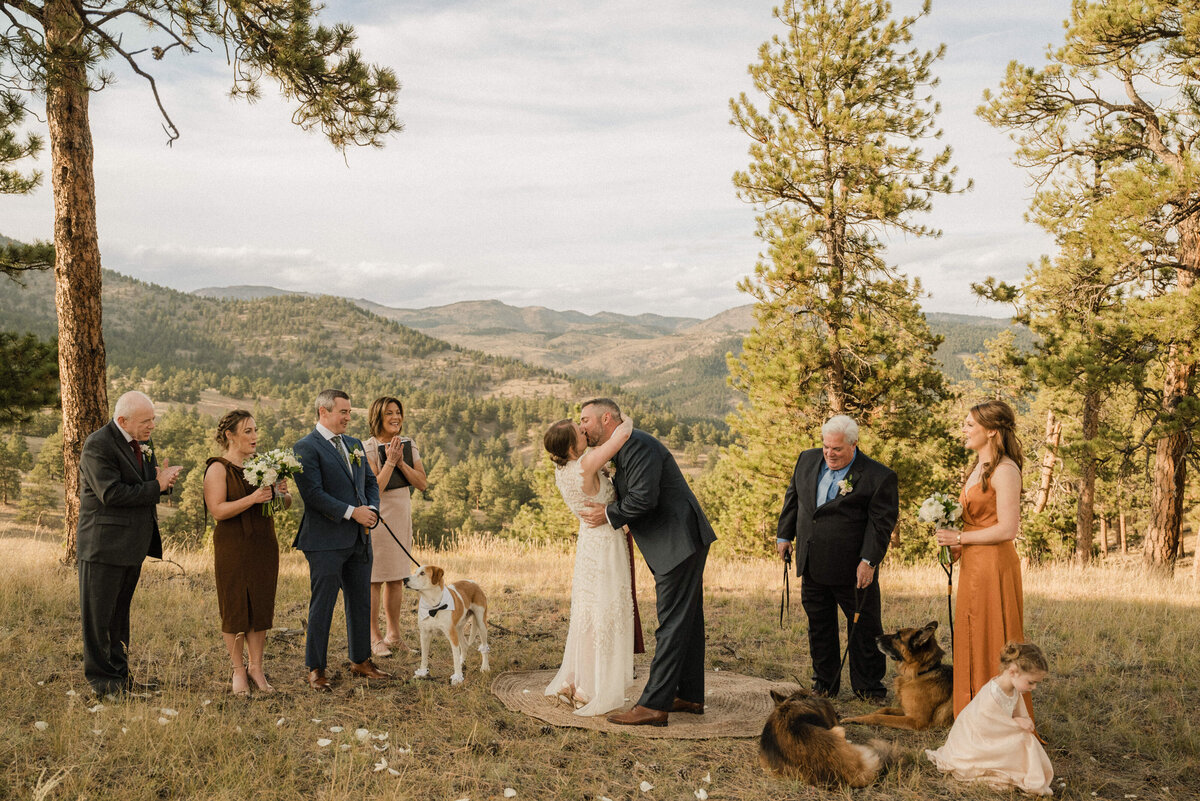 Couple shares first kiss surrounded by family and their dogs at their intimate outdoor elopement ceremony in Boulder