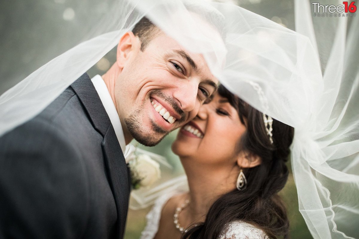 Sweet smiles during a tender moment under the Bride's veil