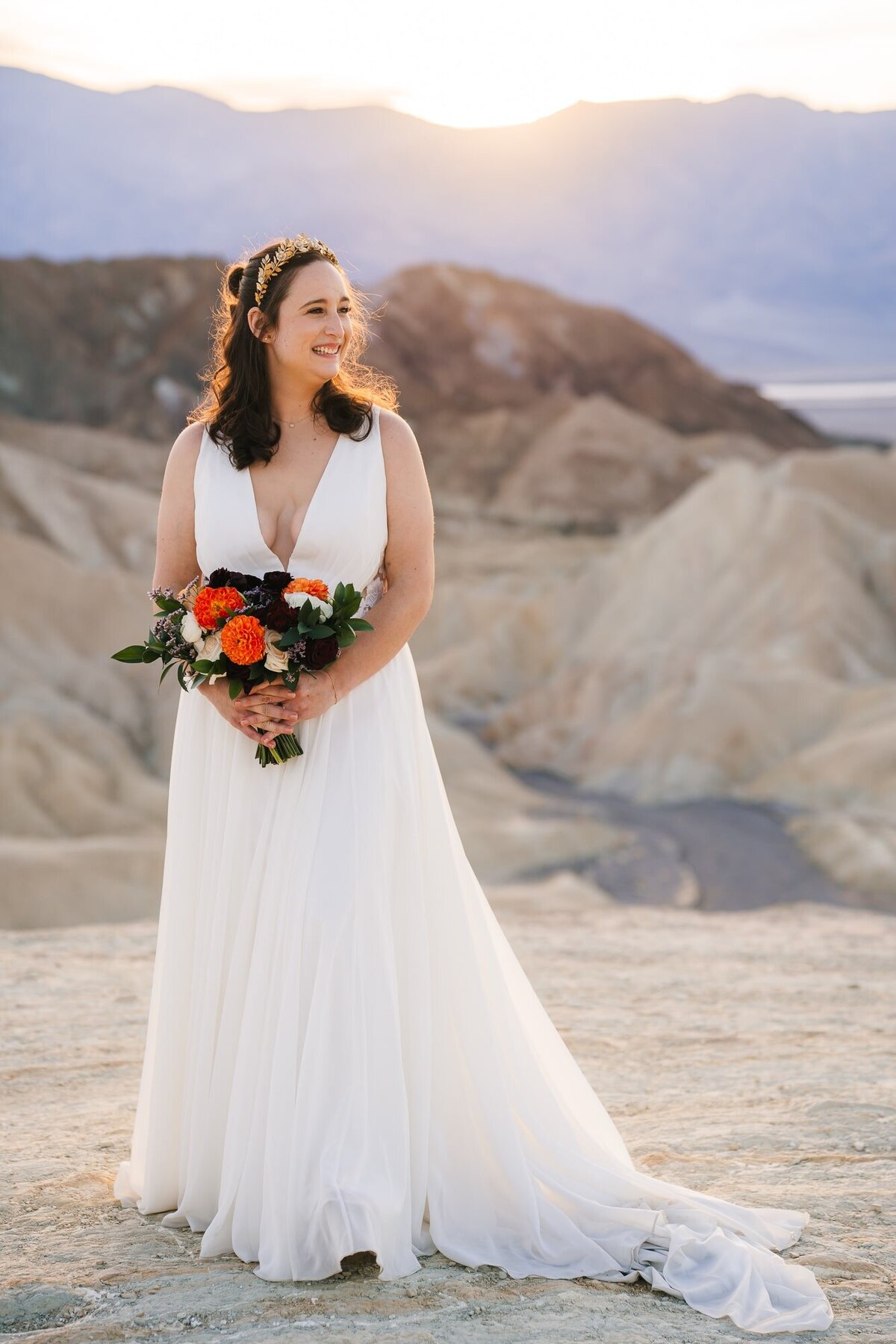 The beautiful bride at Zabriskie Point in Death Valley, gracing the scene in her gown and a radiant smile, holding a stunning bouquet of flowers.