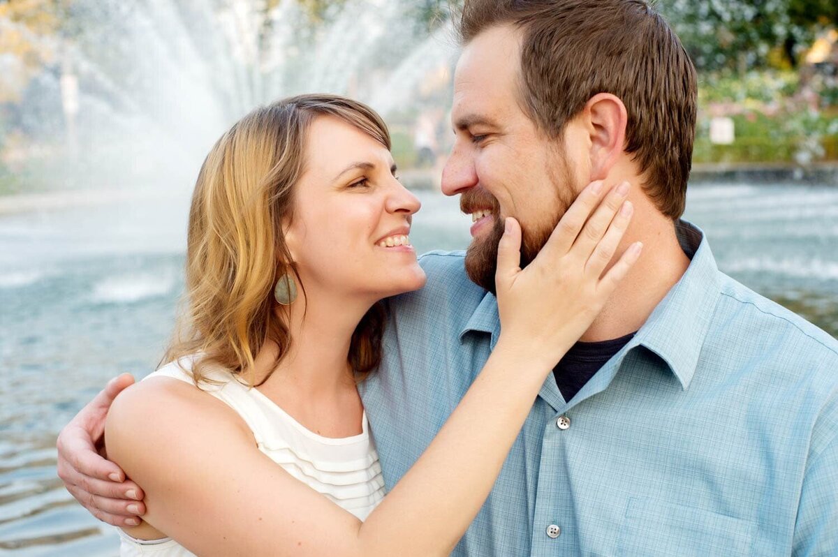 a woman touches a mans face as they sit beside a big water fountain