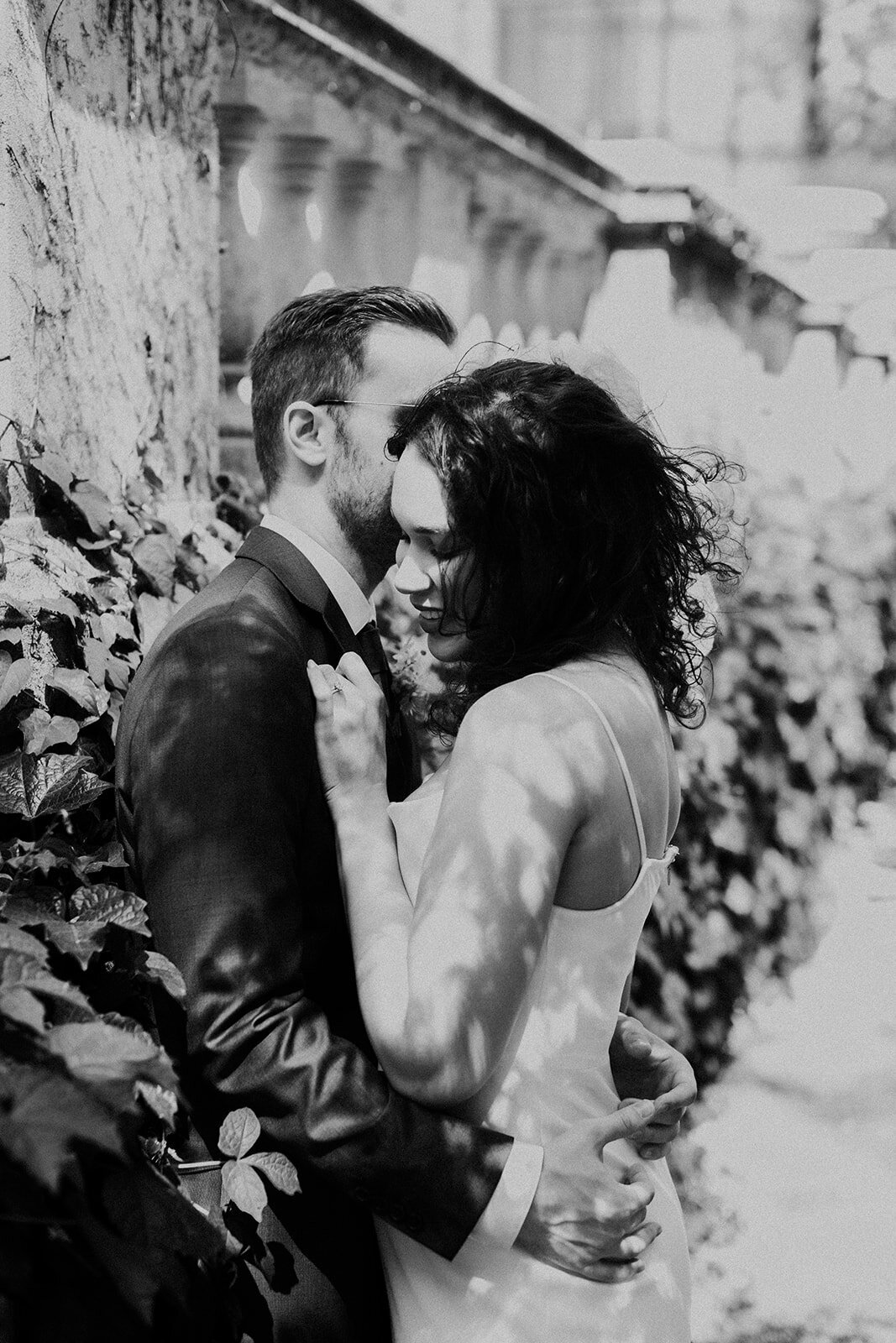 Just Married photo session couple standings in sun dappled garden and embraces as groom whispers in bride's ear