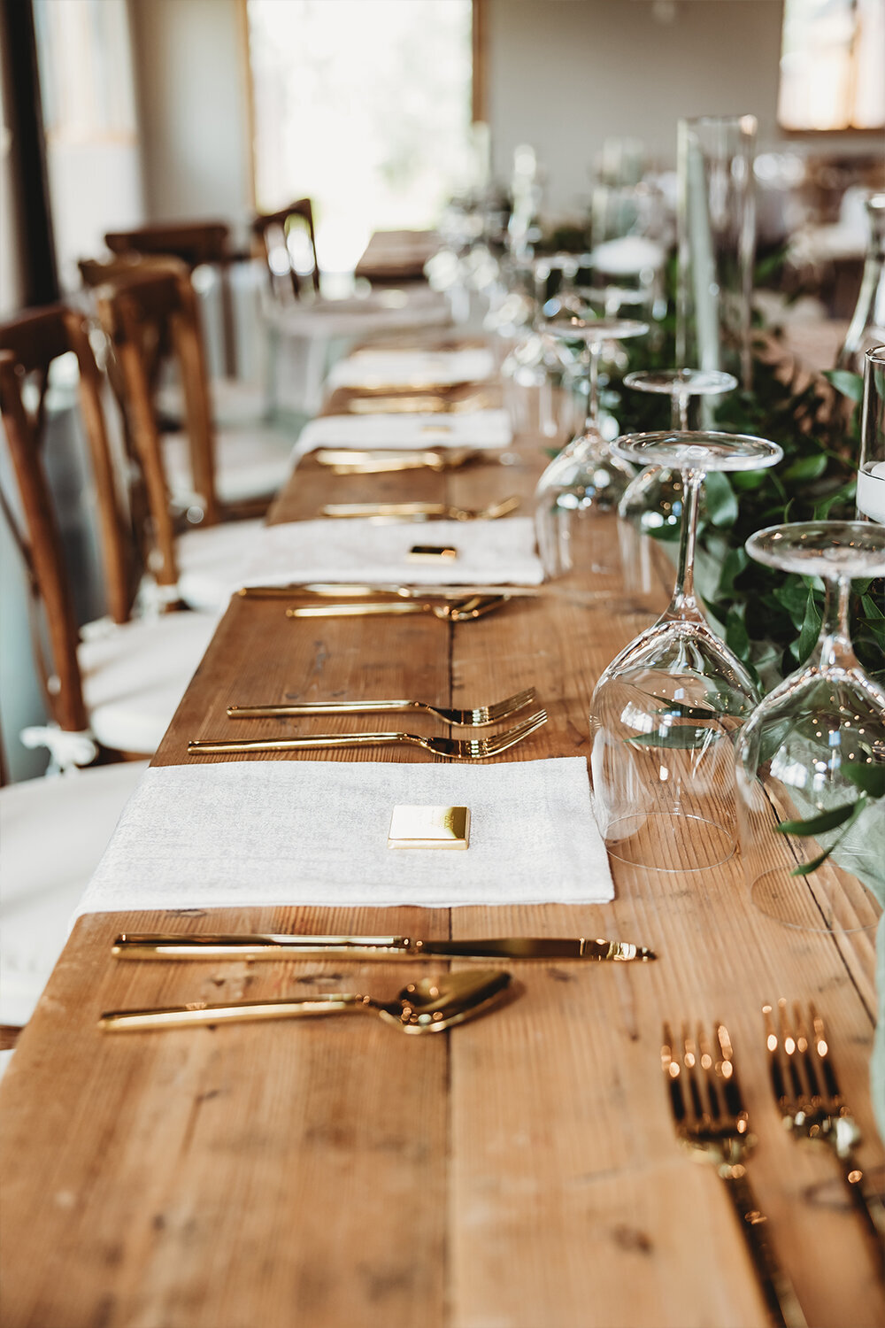 Mountain Sage Wedding table decor at Camelot Ranch: sage green napkins, gold flatware, wine and water glasses, and greenery accents line the center of a rustic, elegant table setting