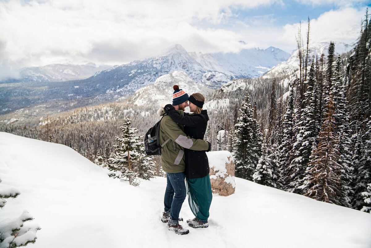 Man and woman in jackets and hats smile in the sow in the Rocky Mountains.