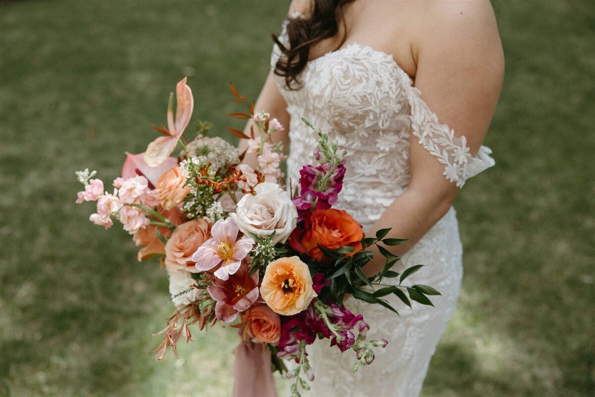 Bridal portrait with bride in lace dress holding colorful bouquet at spring wedding in Longmont, Colorado