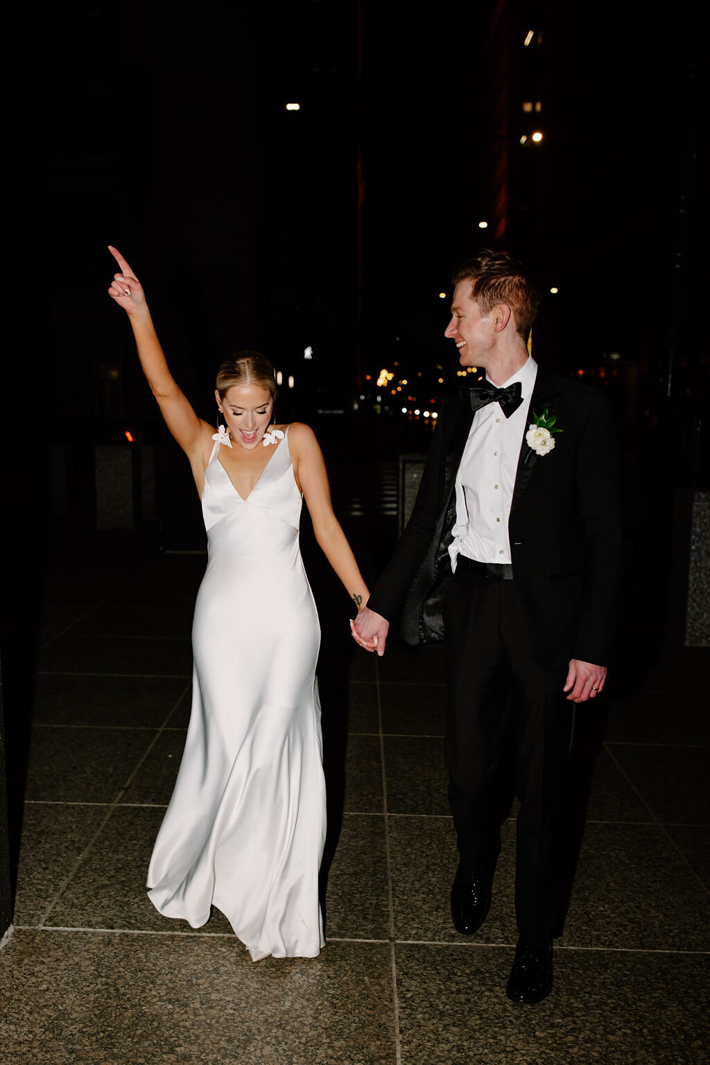 Blonde bride in silky gown dances while holding hands with groom on wedding day.