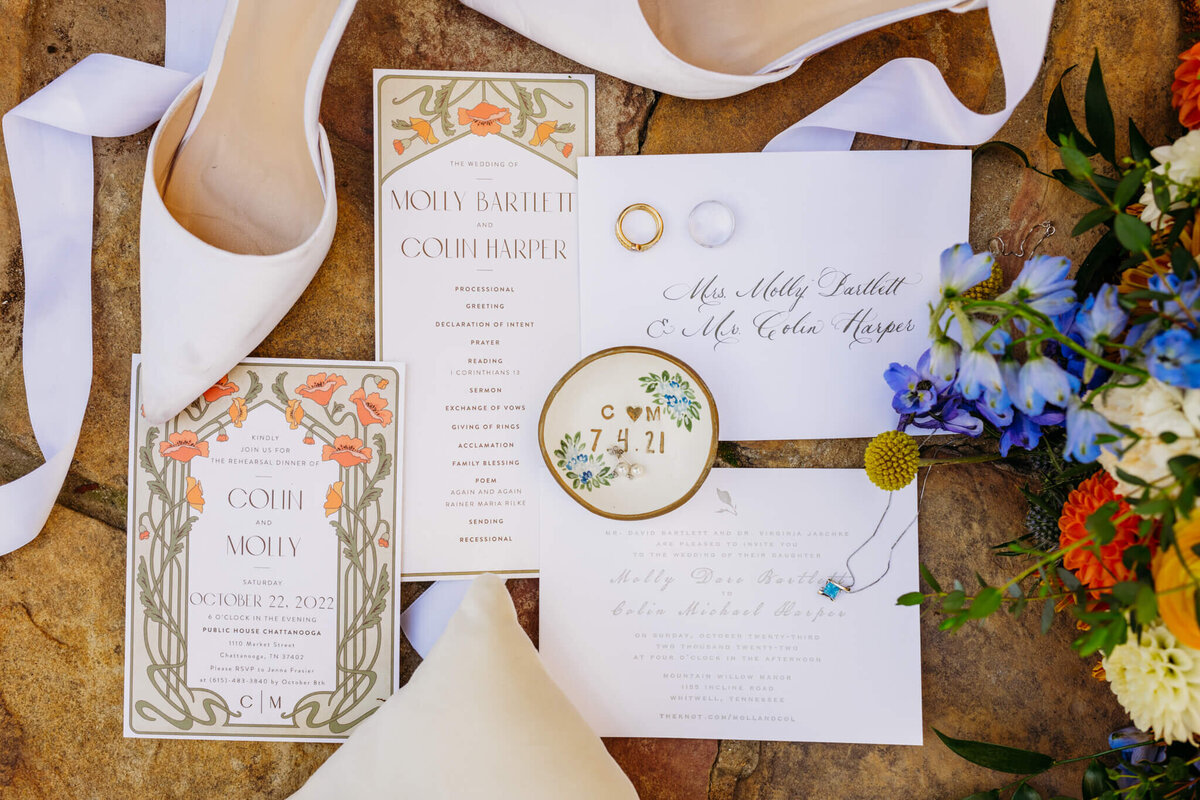 A photo of wedding details including an invitation suite, shoes, rings, and a bouquet