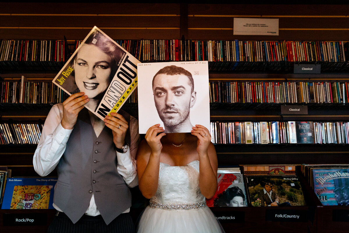 A wedding couple holding vinyl albums up over their faces.