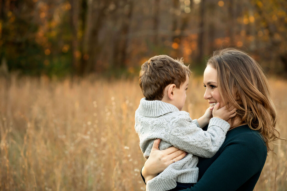 Mother holding young son while smiling at him in field of tall grass