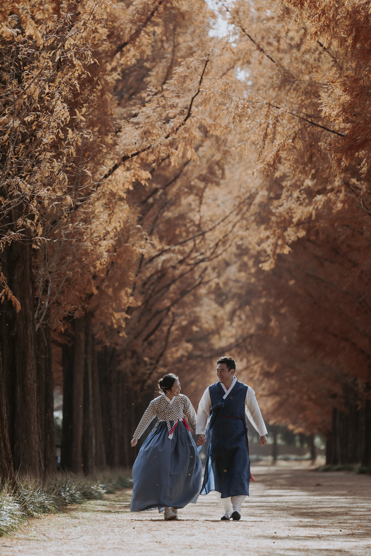 the couple holding hands while walking under the golden metasequioa tress