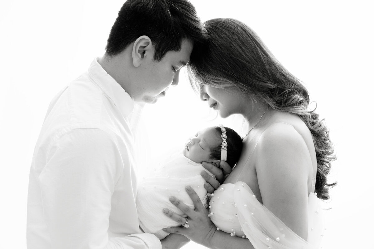A black and white image of new parents holding their sleeping newborn daughter