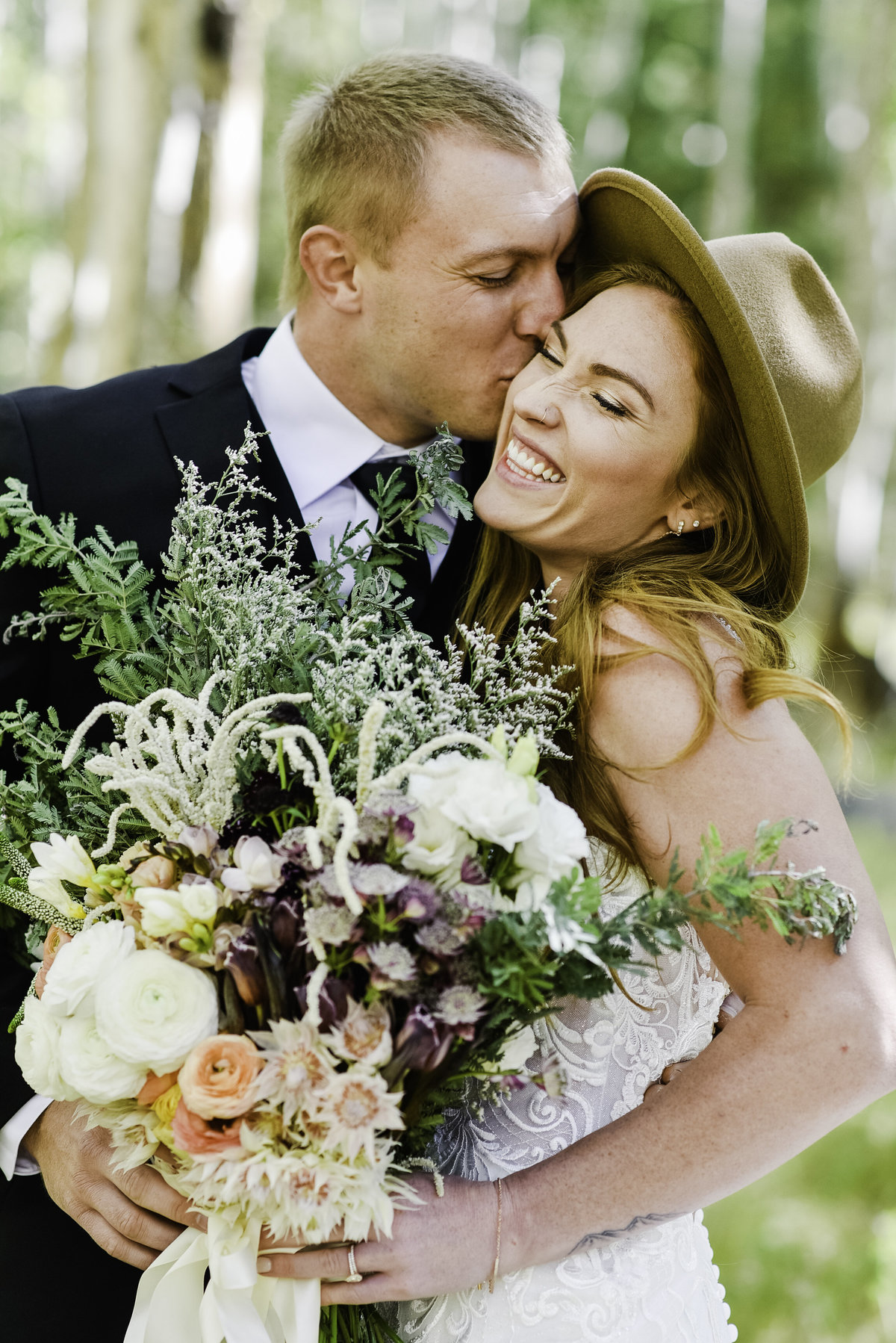 Groom kissing bride wearing hat and holding bouquet wedding Flagstaff aspens