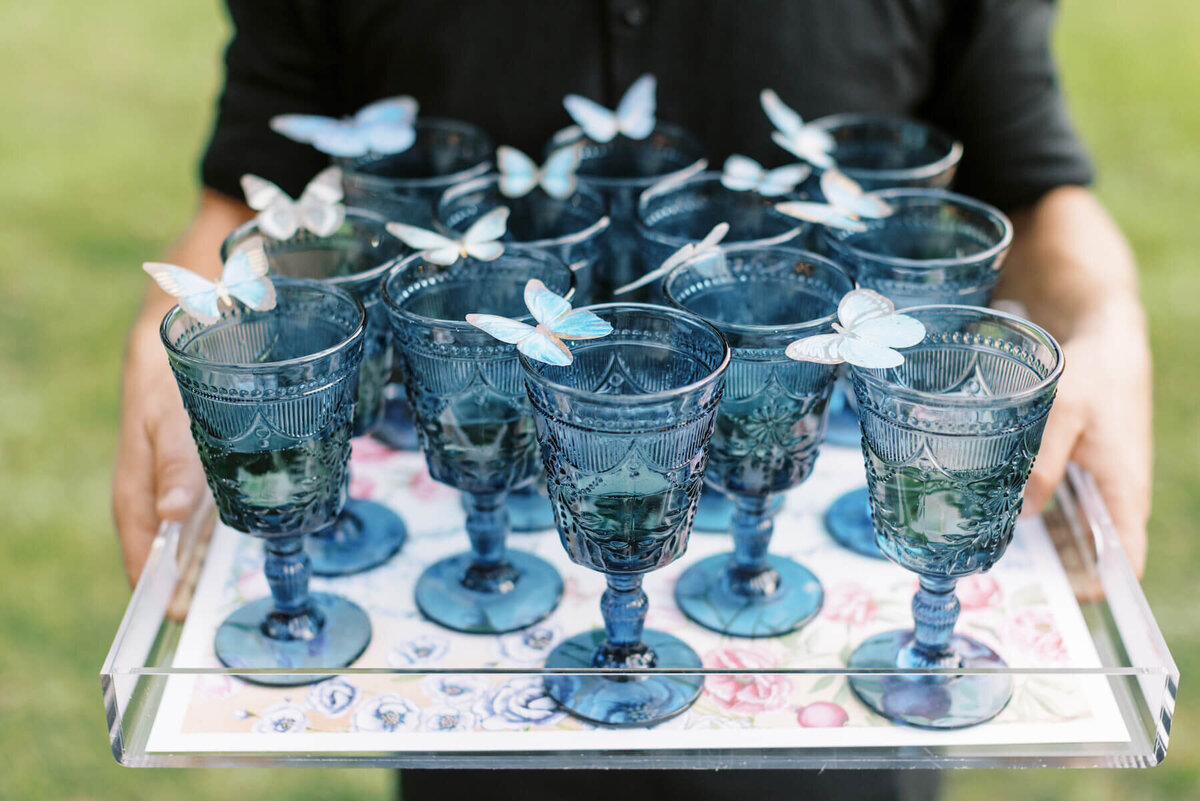 Vintage blue glass goblets filled with champagne and garnished with edible butterflies.