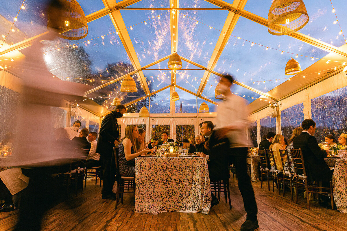 Waiters deliver food in a clear tent at sunset