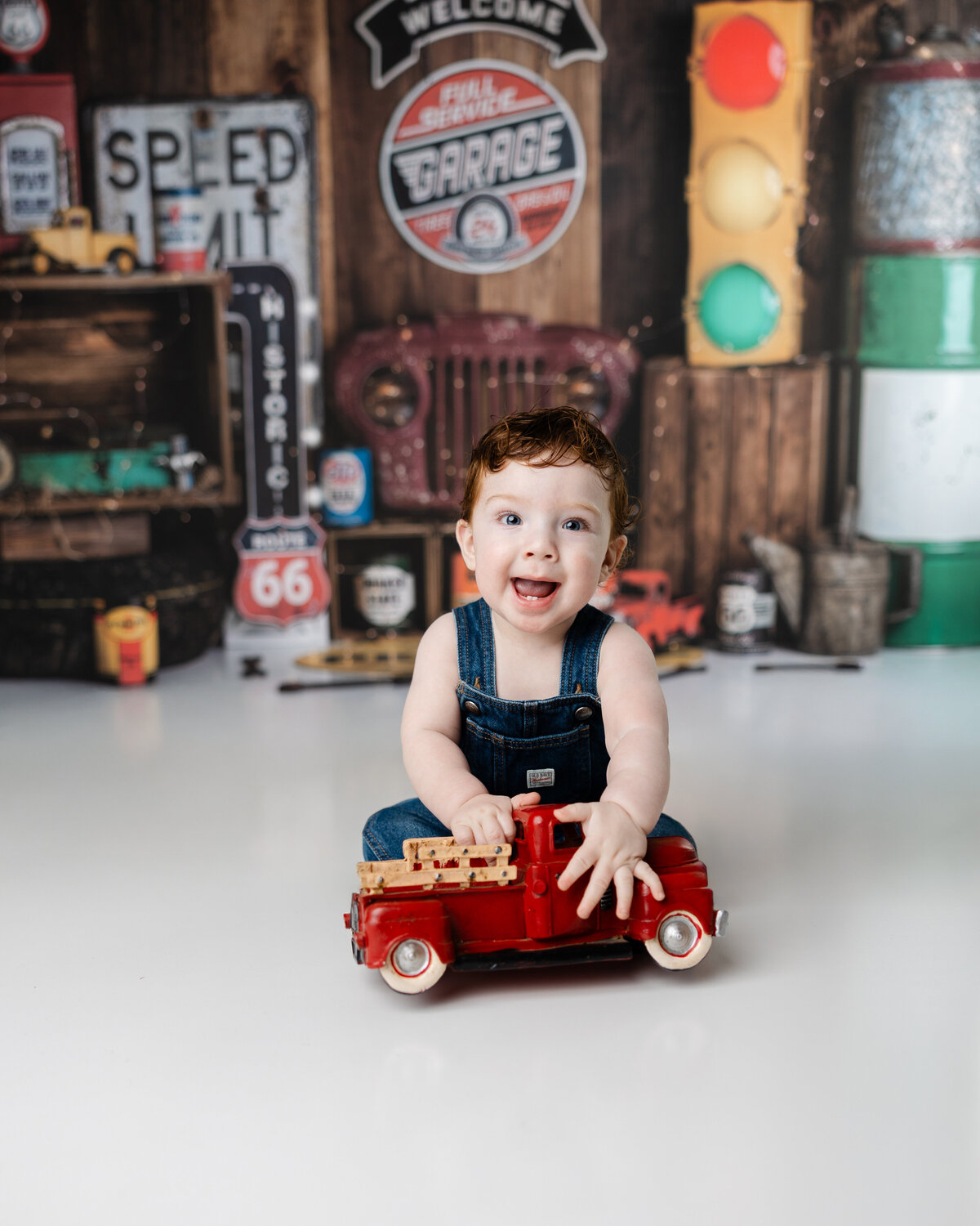 Birthday boy in overalls enjoying playtime in front of a classic car and Route 66-inspired cake smash backdrop.
Photograph by Yucaipa cake smash photographer Kaitlyn Dawn Photography.