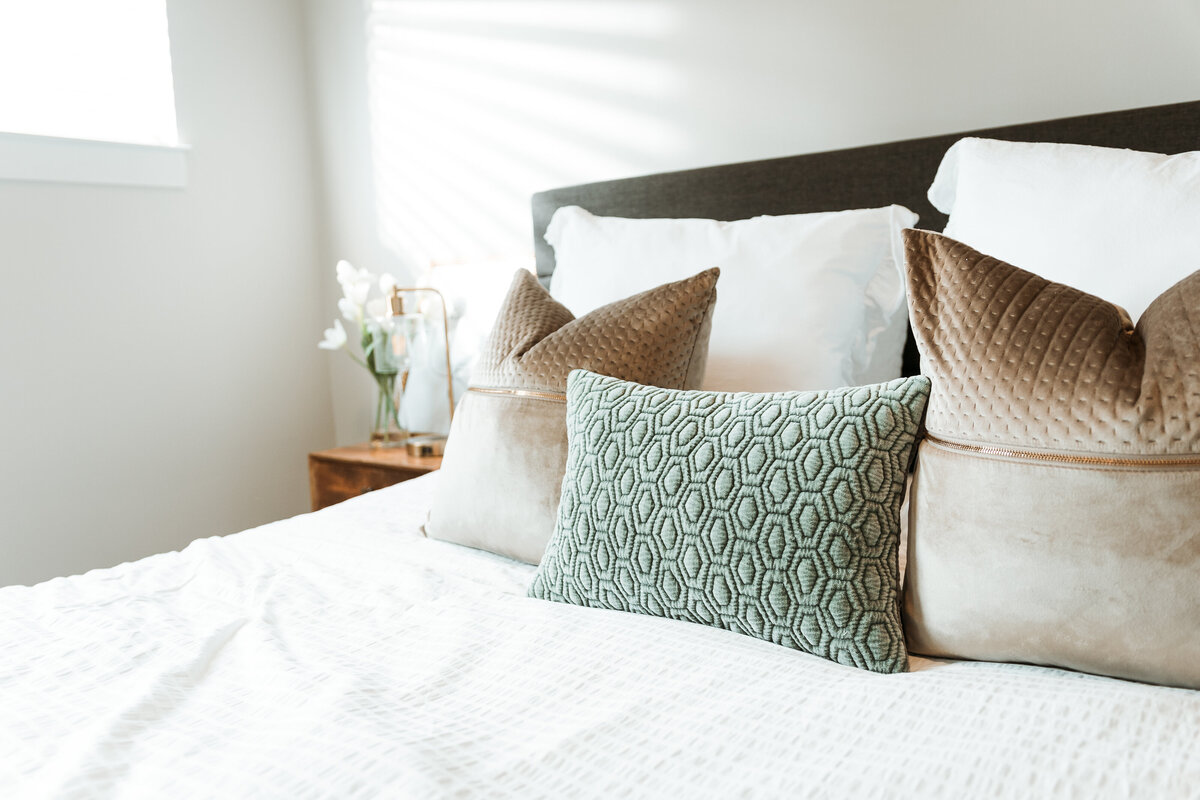 a bed with a white comforter and green and brown pillows
