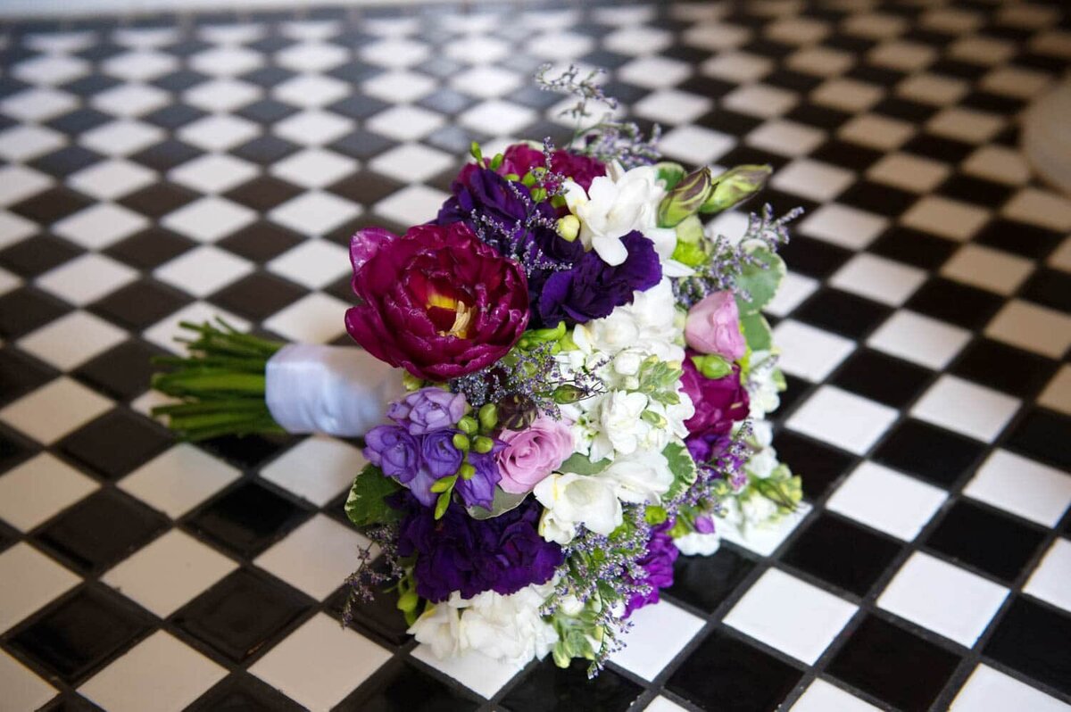 a pretty purple and pink bouquet sits on a black and white checkered tiled floor