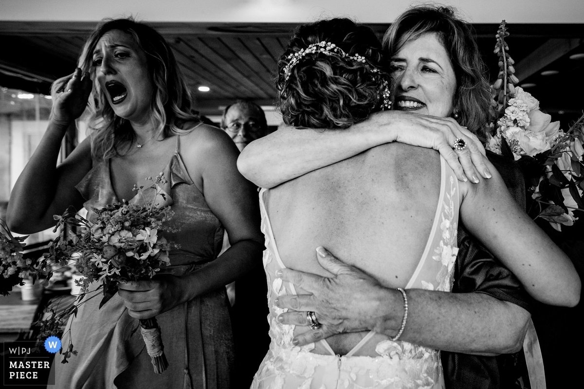 Linekin Bay Resort Wedding the bride hugs her mother in law as a tearful bridesmaid stands next to them at the Maine camp ceremony