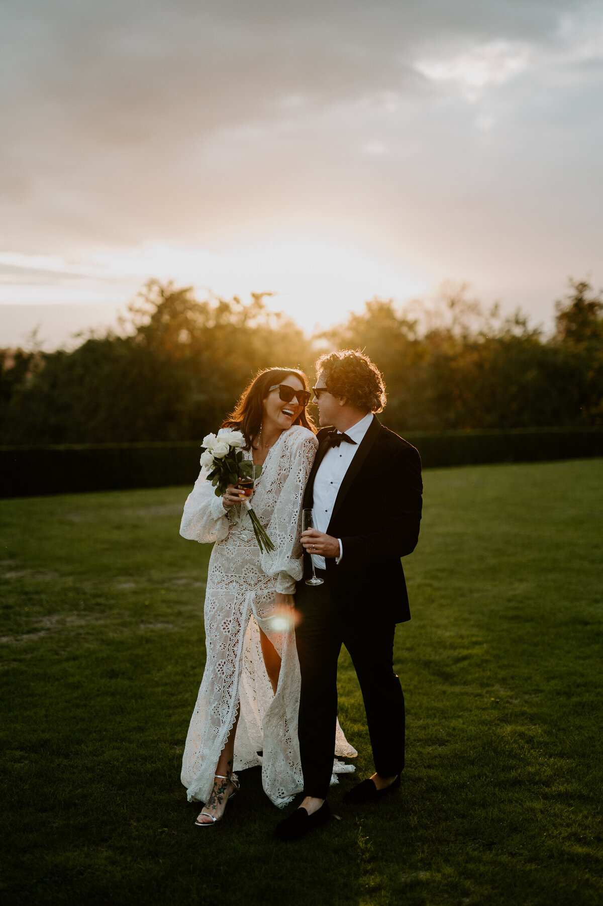 Martine McCutcheon and her husband Jack enjoy a glass of champagne during the sunset at Beaverbrook in Surrey after their vow renewel. Martine is wearing a white dress and sunglasses and carrying flowers whilst jack is wearing a black tux and sunglasses.