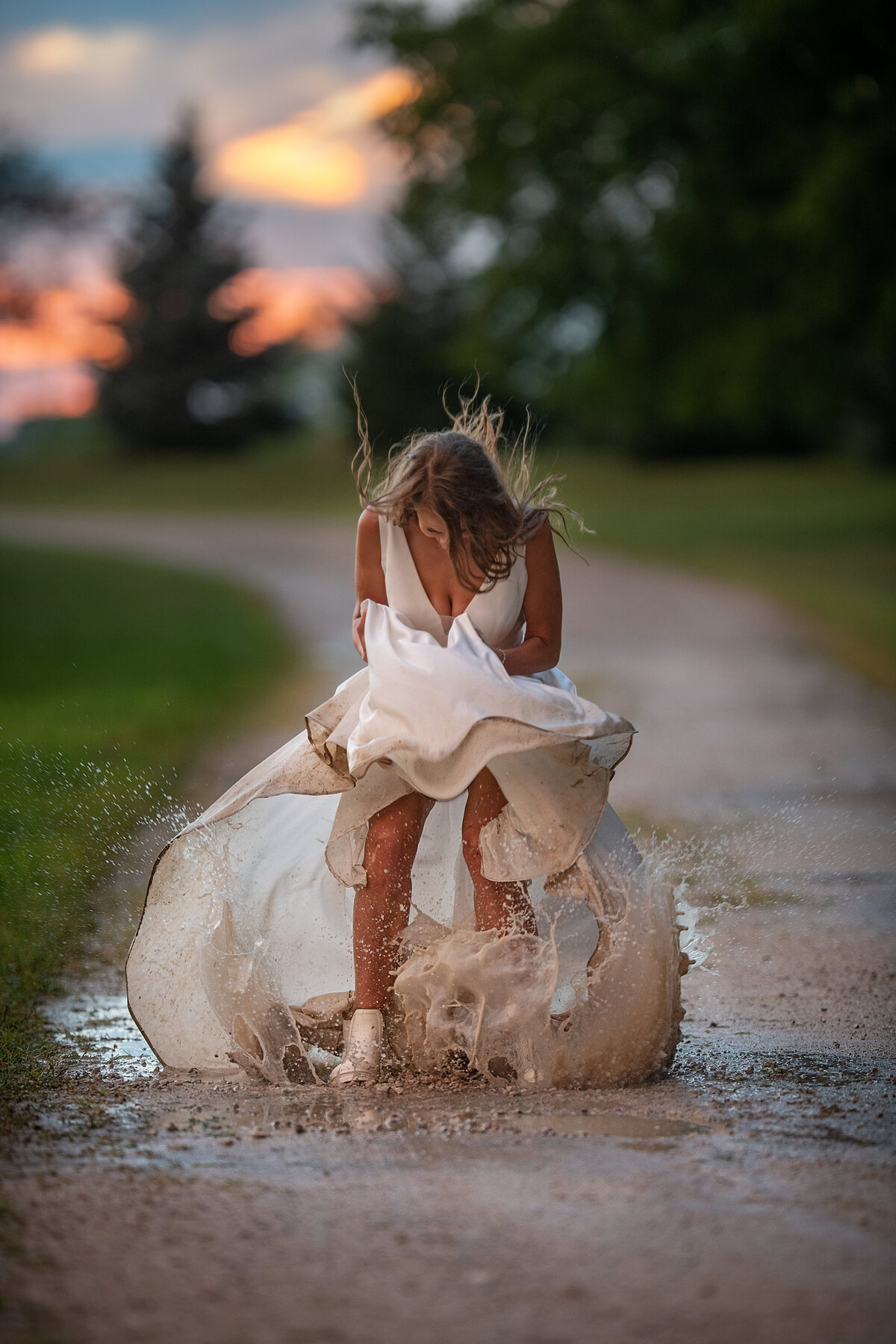 Bride is splashing in a muddy puddle with a white wedding dress during her rainy wedding day