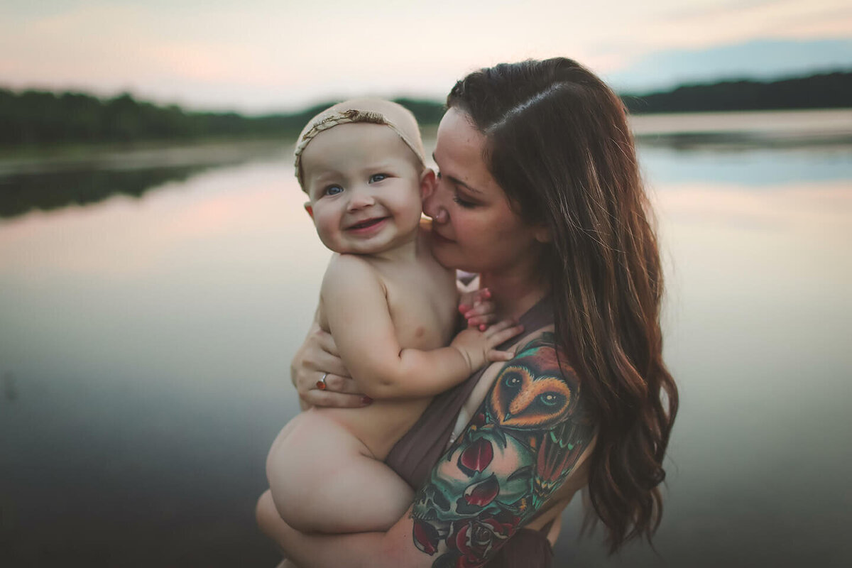 Mother holding naked baby by the lake