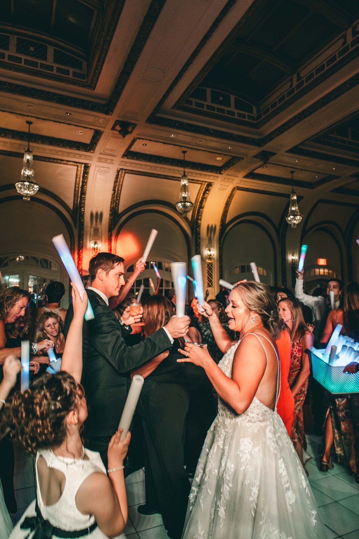 Bride and groom dancing joyfully with guests waving light sticks at a lively wedding reception in an elegantly decorated hall at Park Farm Winery.