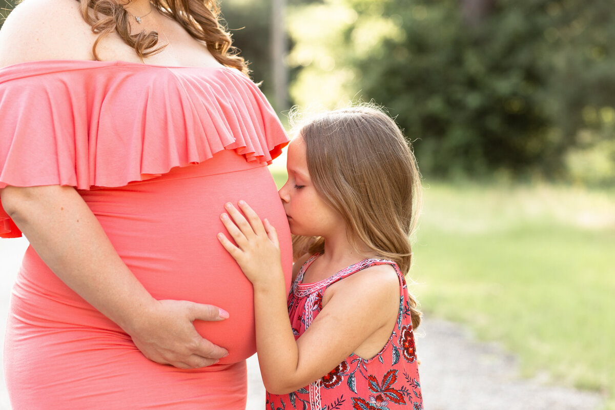 girl embraces expectant mother in a coral gown