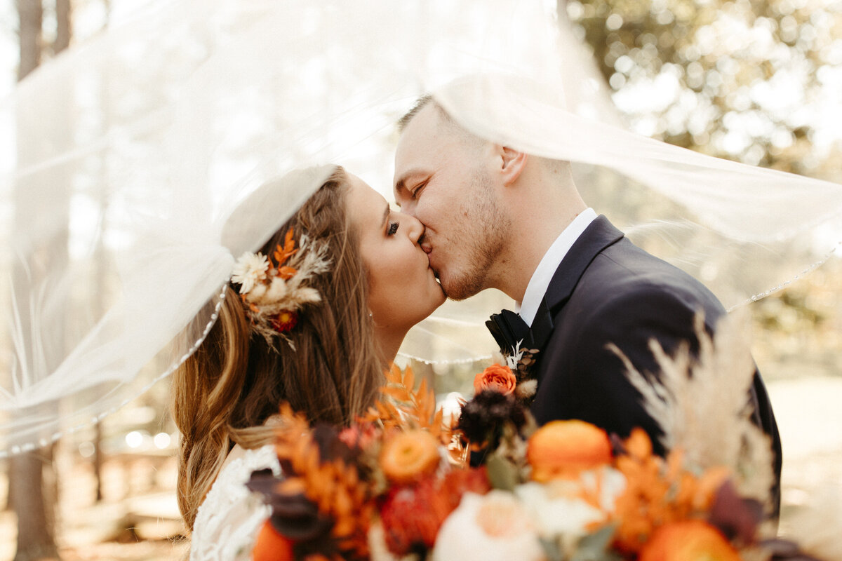 Bride with fall flowers in her hair kissing her groom under her veil