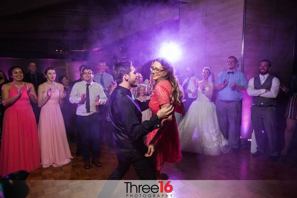 Guests dance in the middle of the floor during a wedding reception as the Bride, Groom and other guests cheer them on