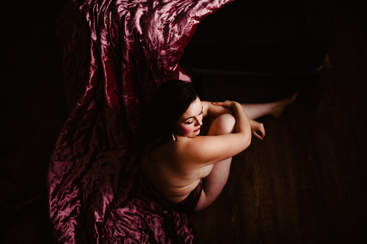woman with knee up sitting on pink velvet bedspread