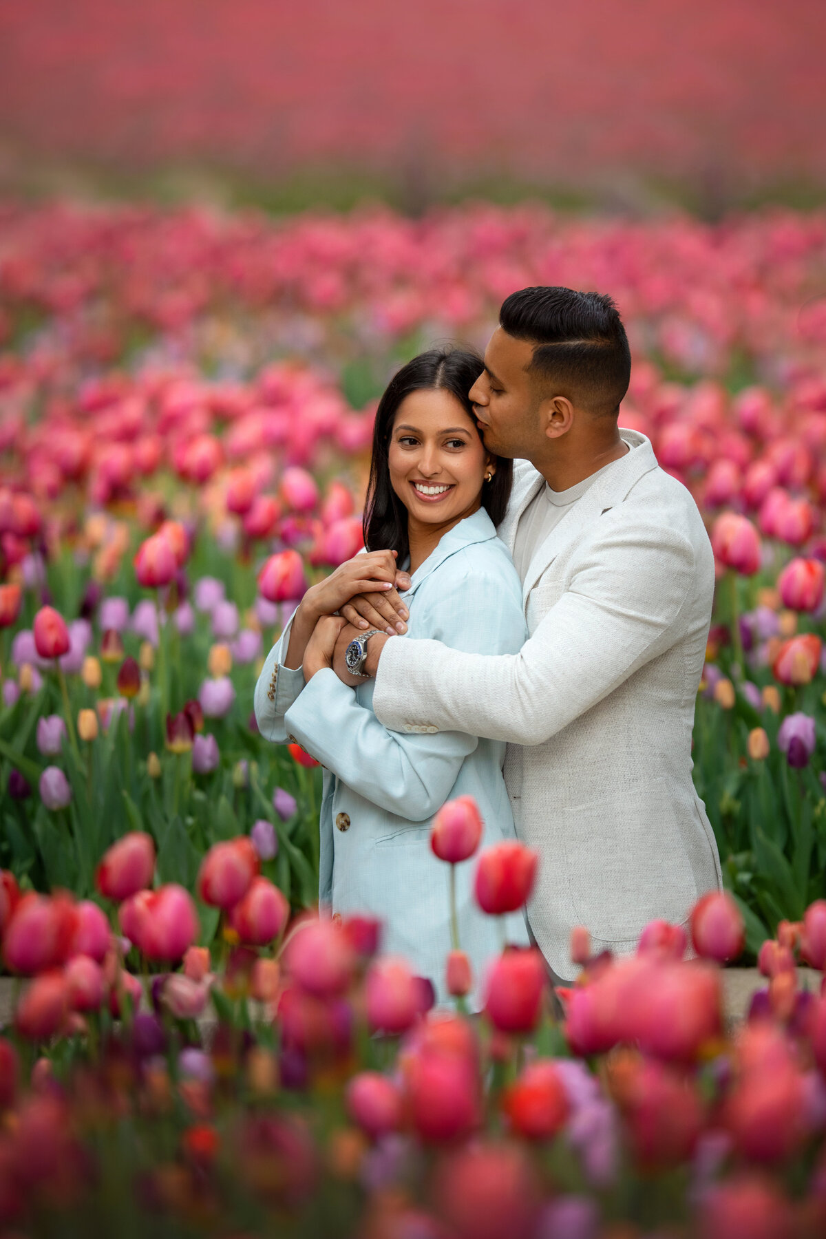 Engaged Indians in light color suits  hugging in the see of tulips in downtown Chicago