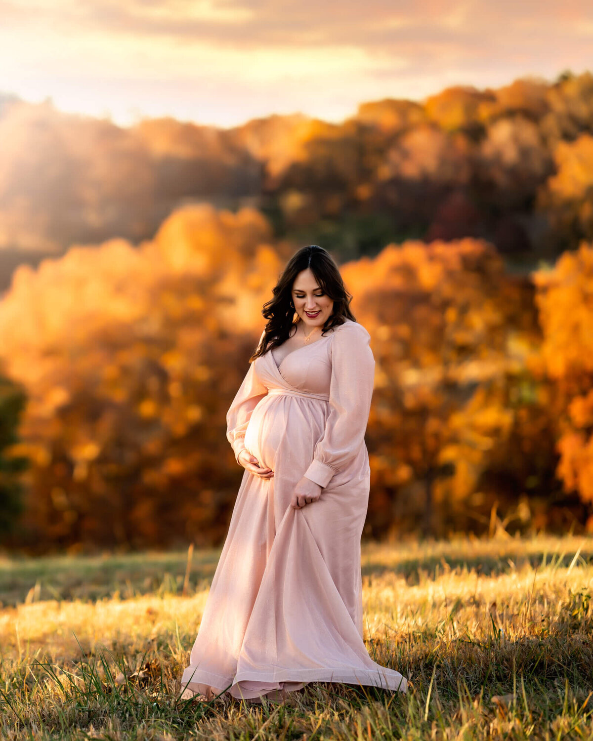 A beautiful, expecting woman swishes her long pink dress and laughs as the sun sets behind her