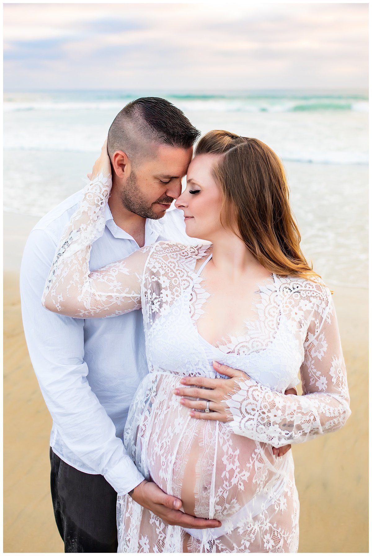 Couple snuggling while holding pregnant belly for a beach maternity portrait in San Diego