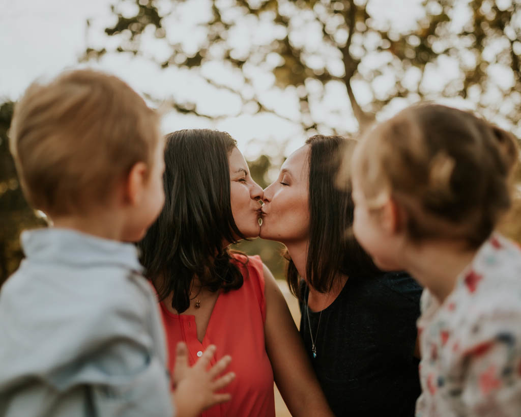 LQBTQIA family photo of two moms kissing with kids watching