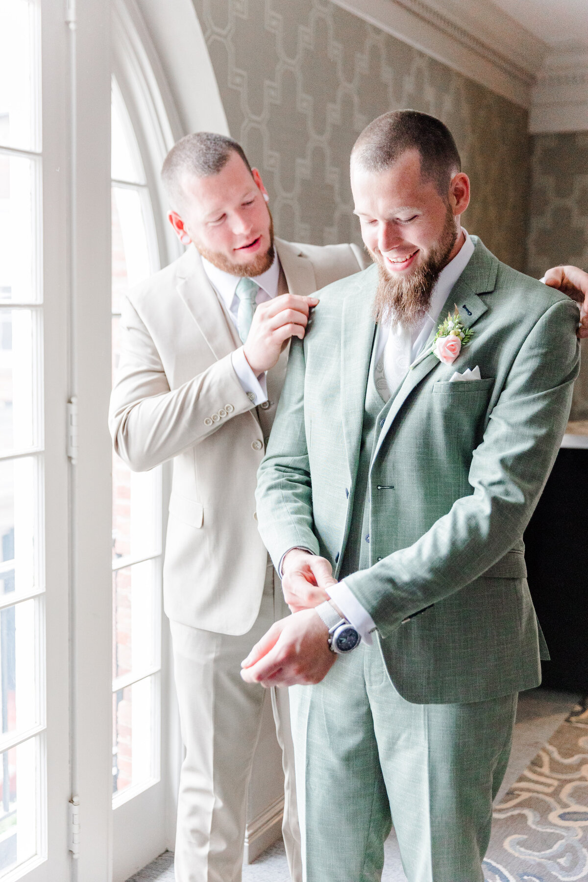 groomsman helping groom adjust his suit jacket