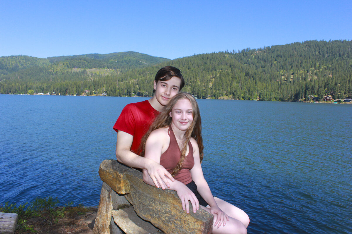 Photo of a young lady  and  young man sitting on a bench with lake in background