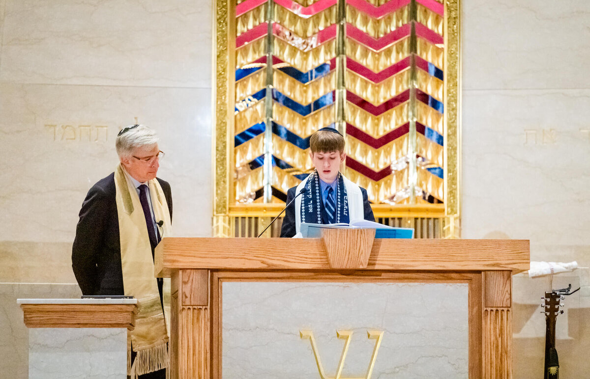 A rabbi watches from the side of the bimah as a boy performs his haftarah