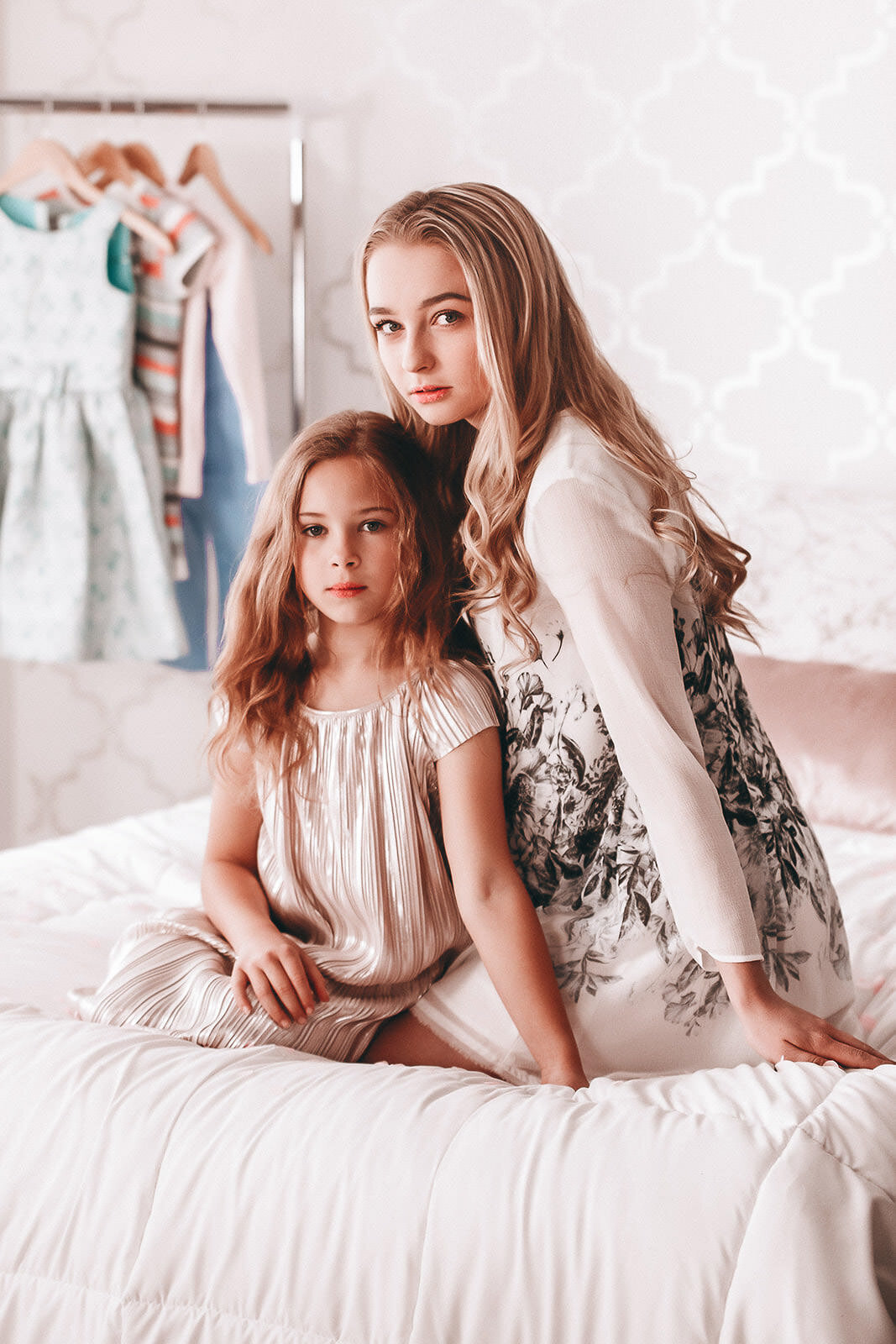 two sisters sitting on a bed in front of closet