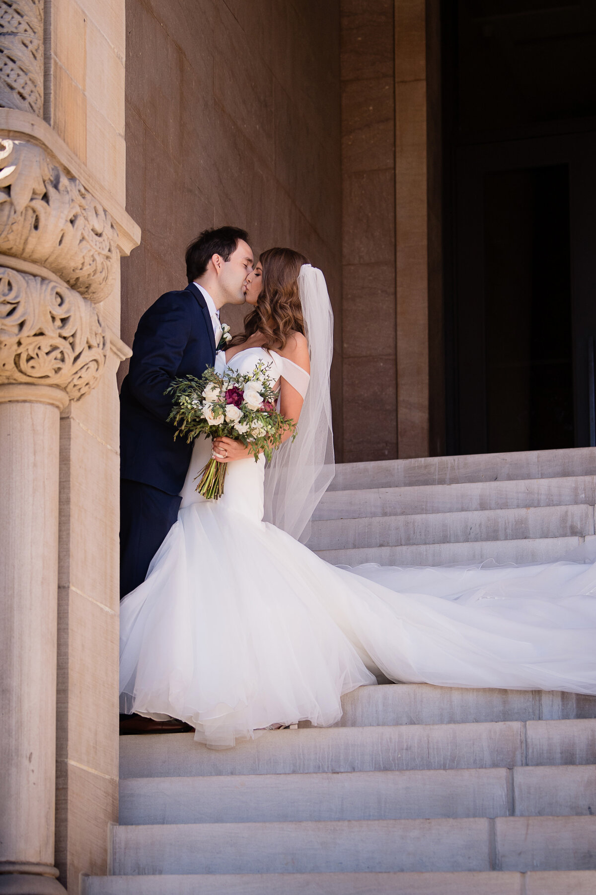bride and groom kiss on stone steps by pillar
