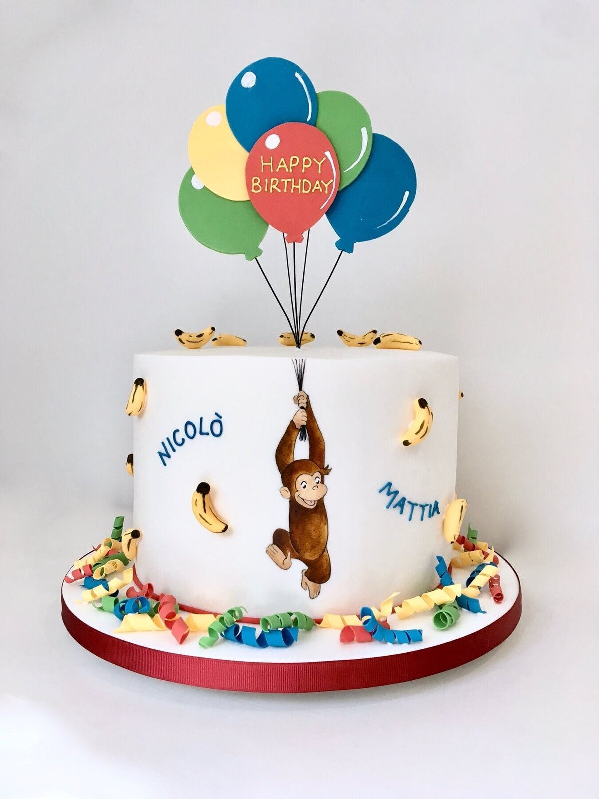 A fun birthday cake with a hand painted monkey hanging off of string with balloons coming out of the top of the cake connected to the string and banans all over the cake