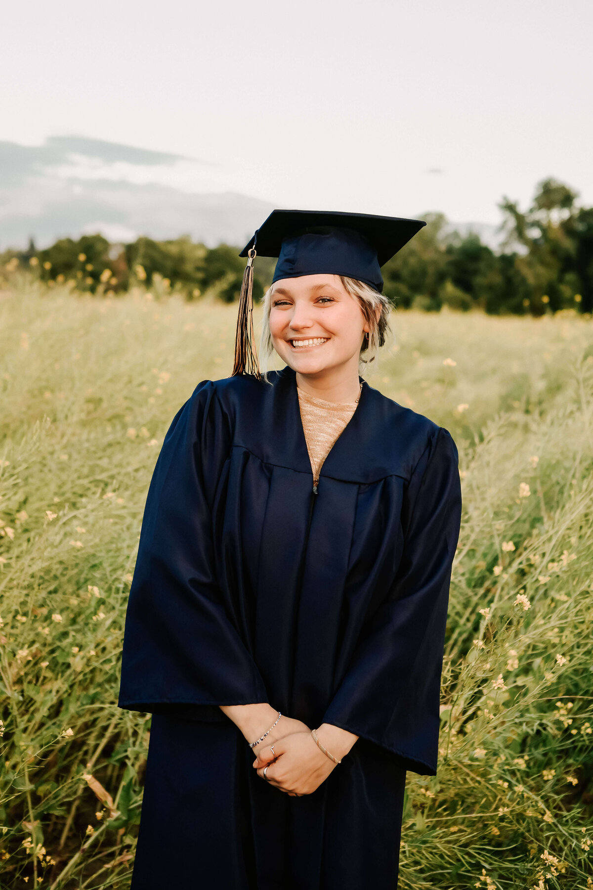 A West Albany High School graduate poses in a field for senior portraits. She's wearing a dark blue cap and gown.