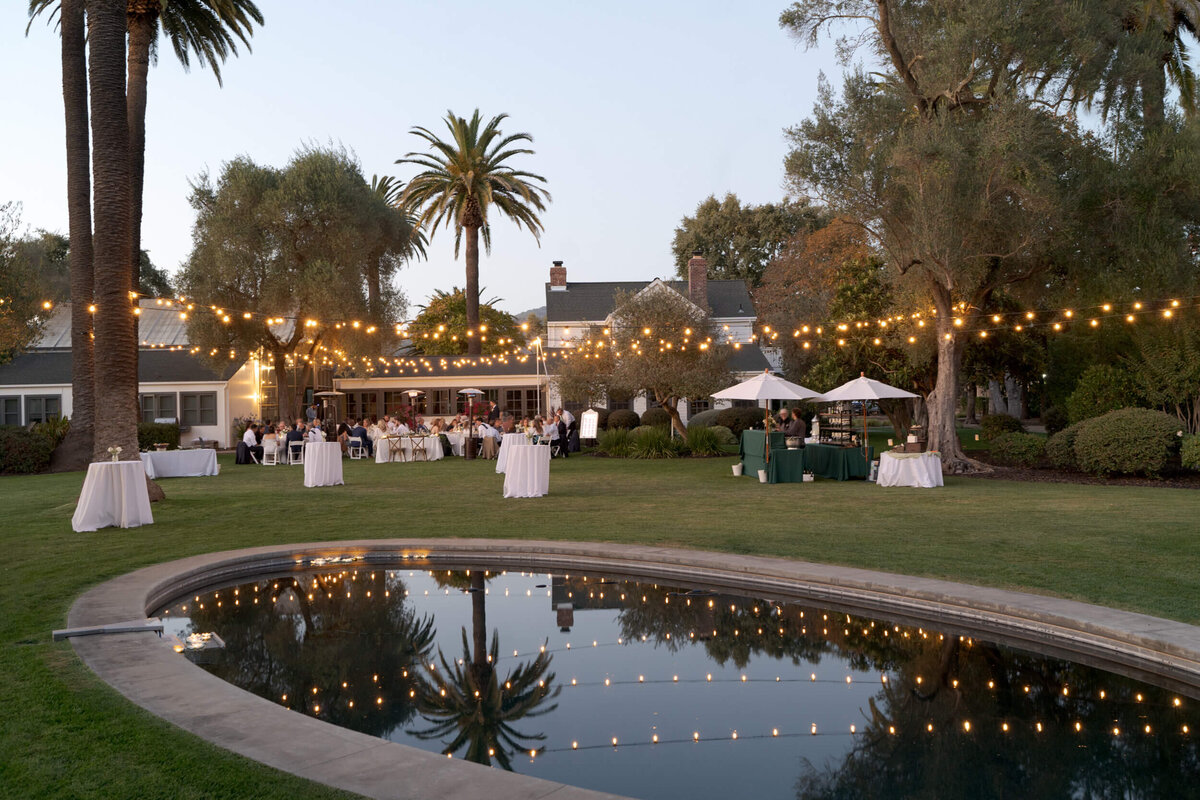 Wide shot of an outdoor wedding venue by the pool with warm yellow lights.