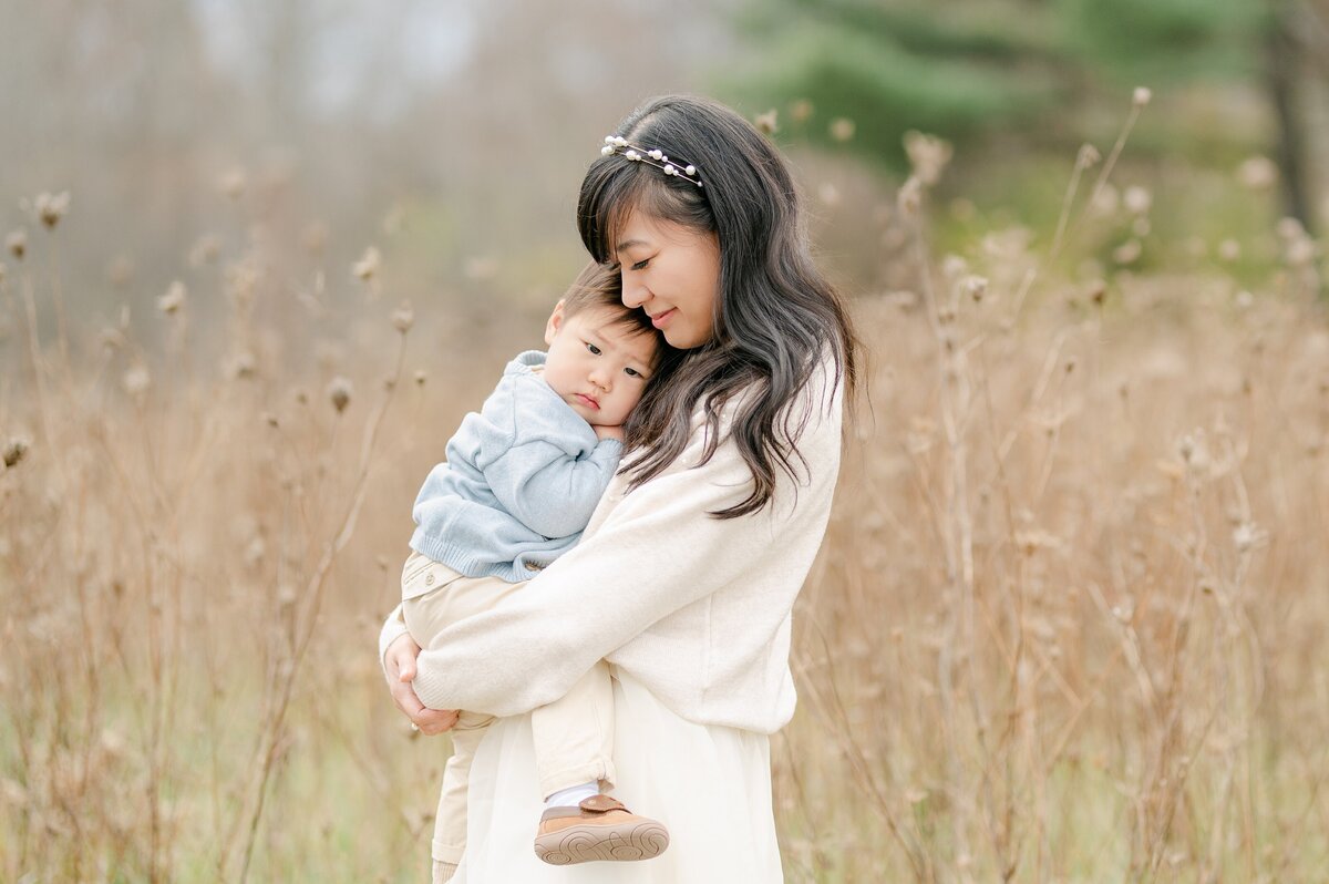 Mom snuggles her son while standing in tall grasses