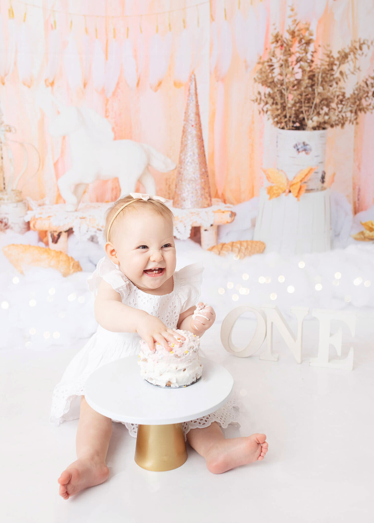 Baby girl laughing while digging into her cake at LA cake smash photoshoot - By Los Angeles Newborn Photographer