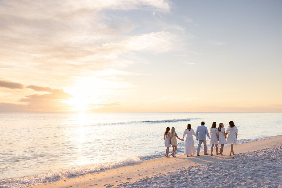 A family holding hands and walking along a beach at sunset.