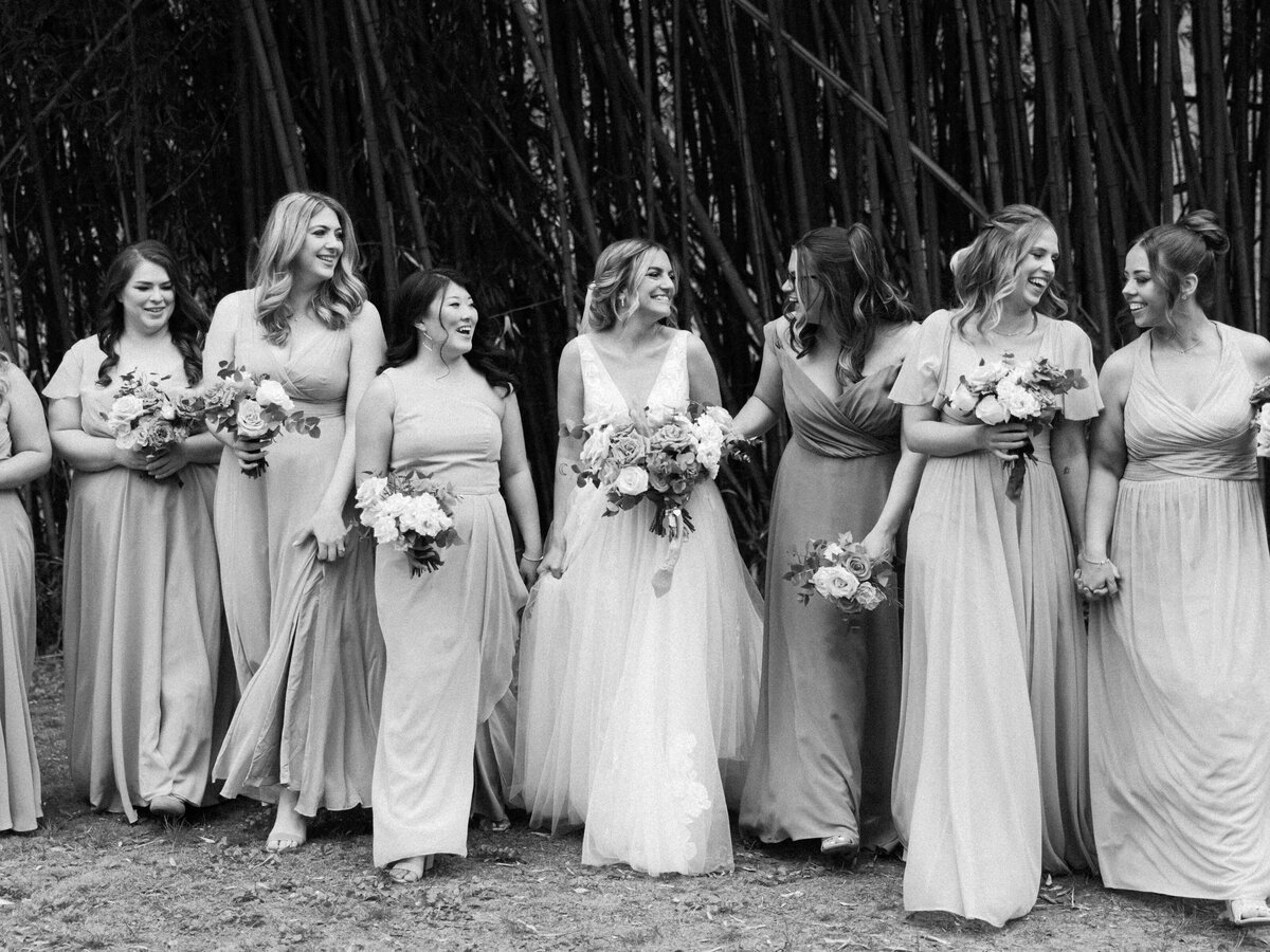 A group of bridesmaids walk together while they laugh and smile at one another