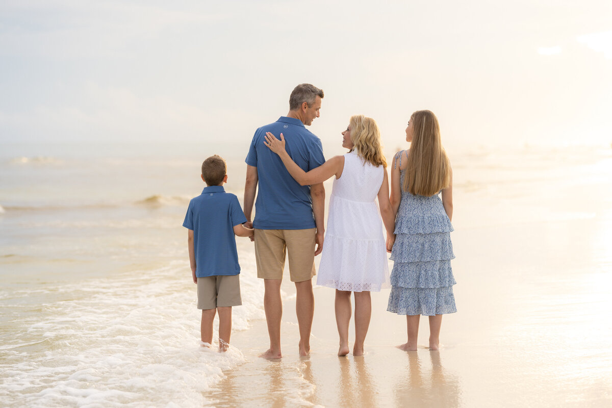 A family of four standing at the beach with the waves at their feet on 30A.